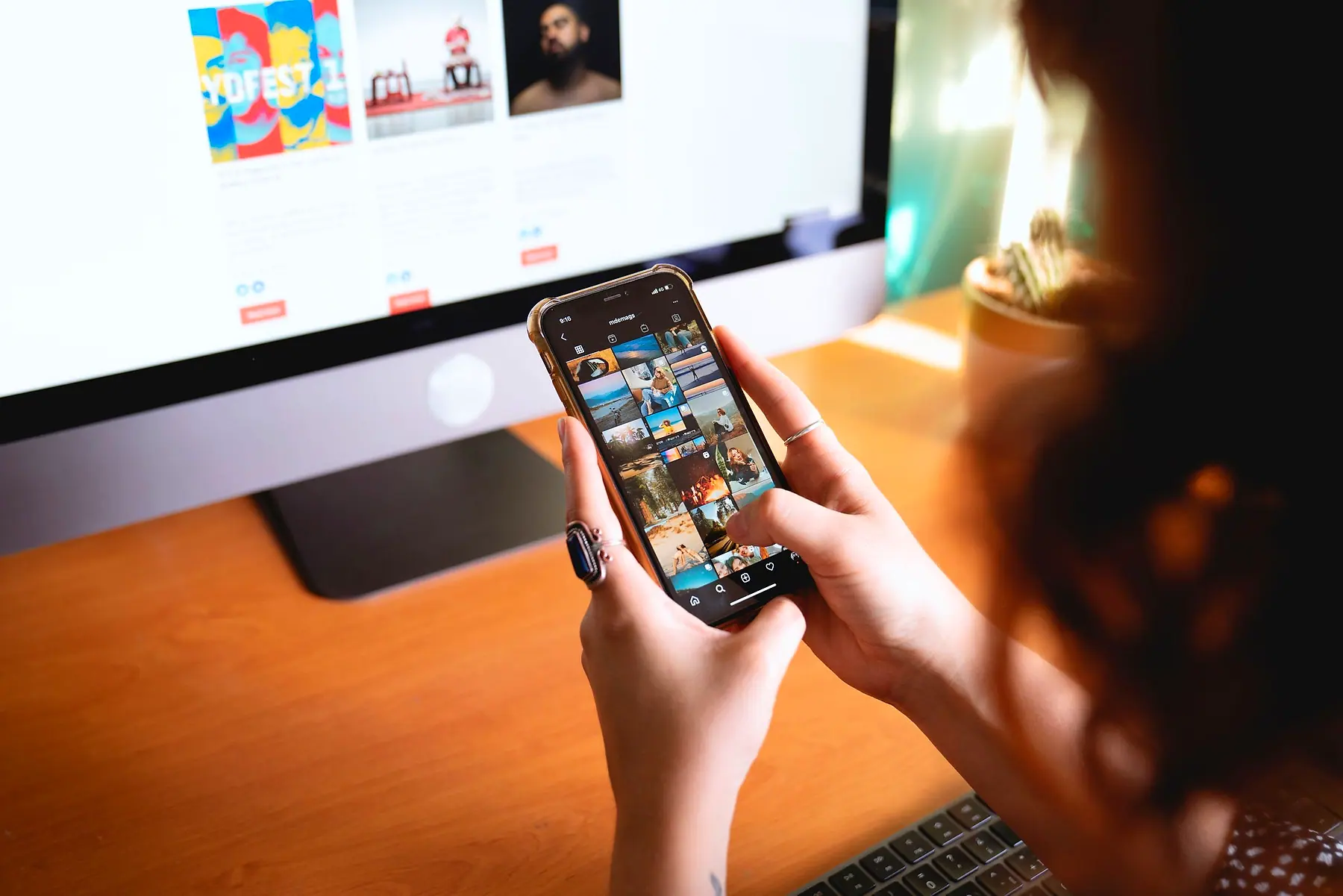 Hands scrolling a social media feed on a phone at a desk