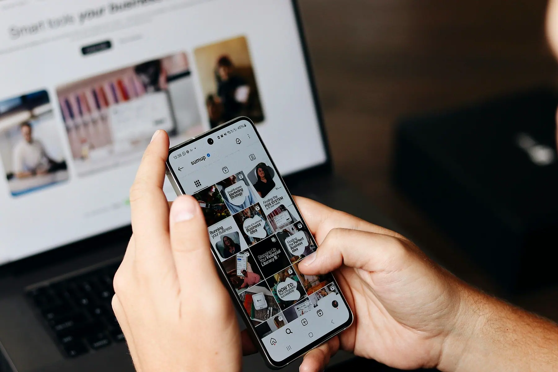 A hand holding a phone showing a mobile website in front of a laptop