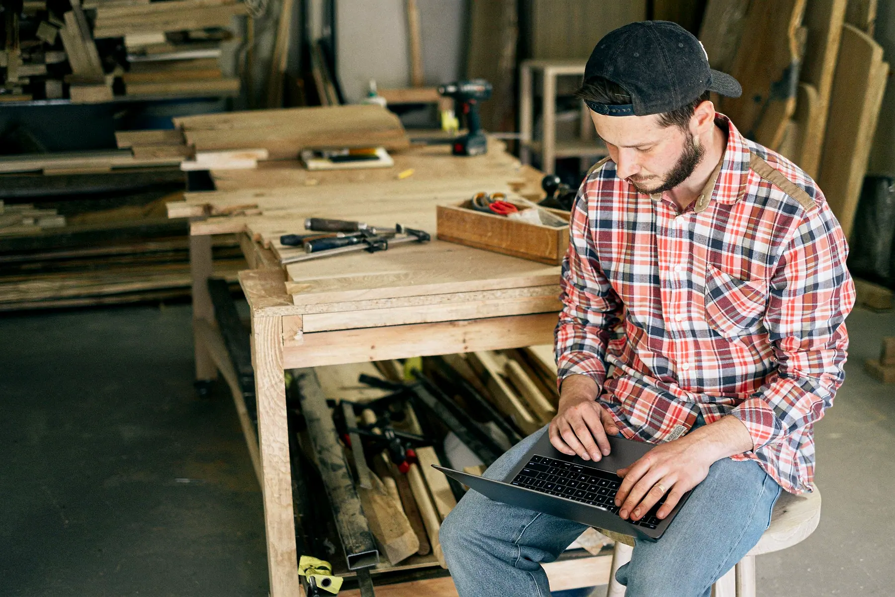 A carpenter sitting in his workshop working on a laptop