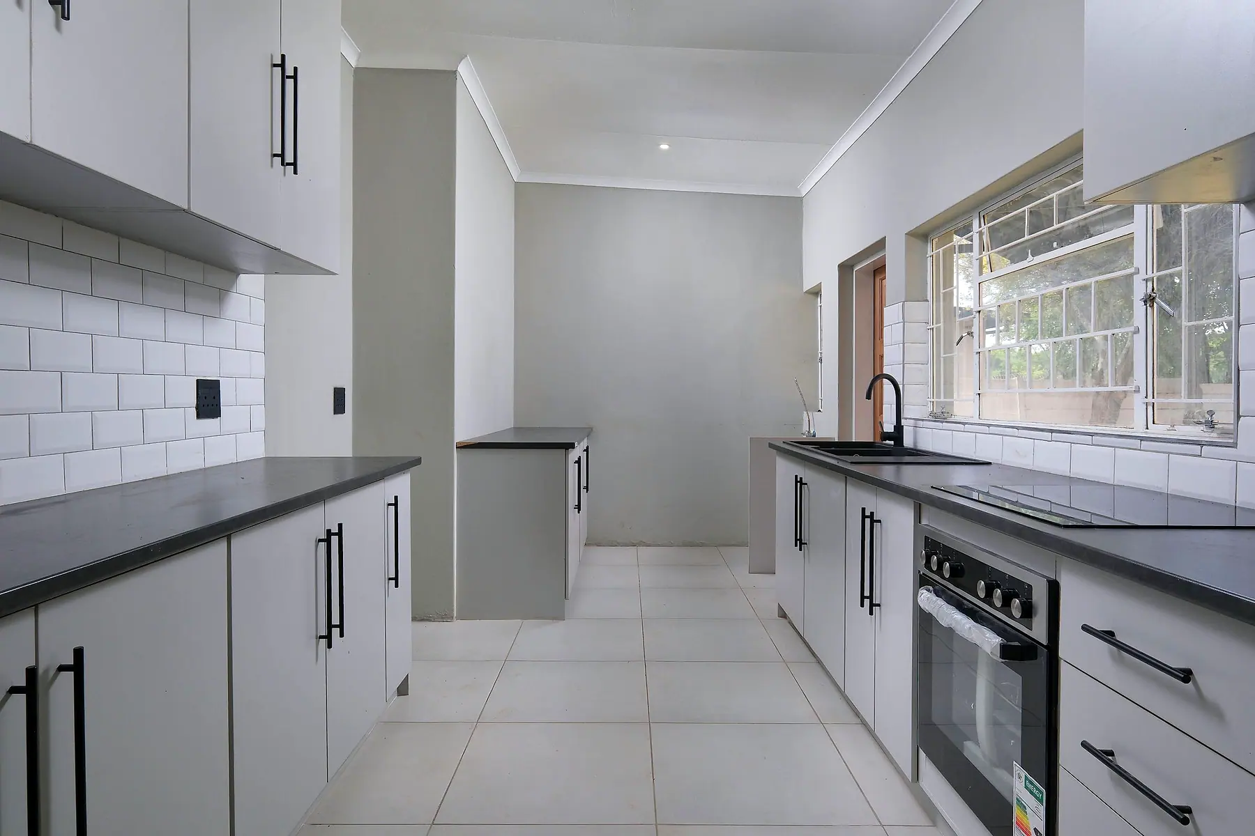 A newly finished kitchen with grey cabinets, a white tiled splashback and a built-in oven