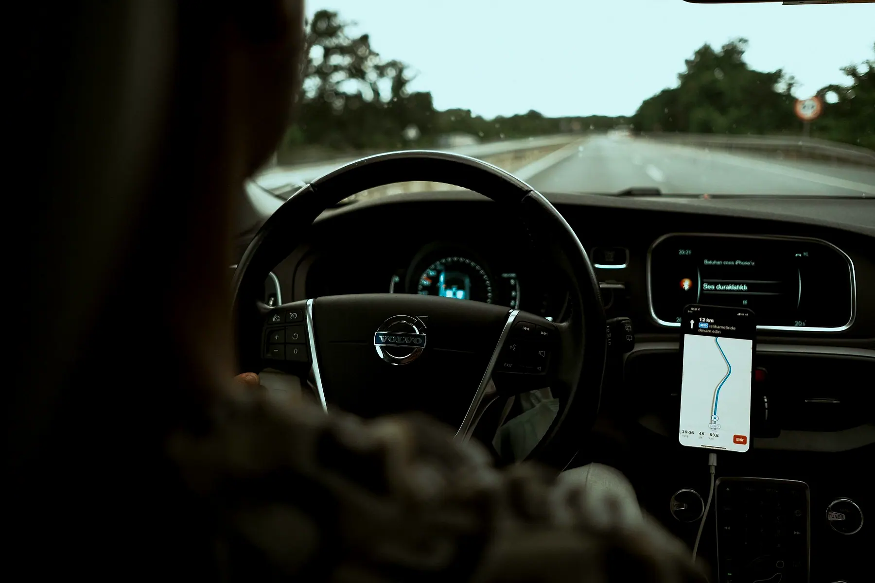 A driver's view of the steering wheel with a phone in a dash mount showing a map route
