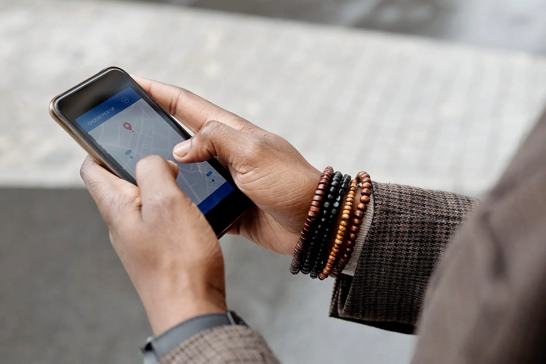 Close-up of hands with beaded bracelets using a map app on a phone outdoors