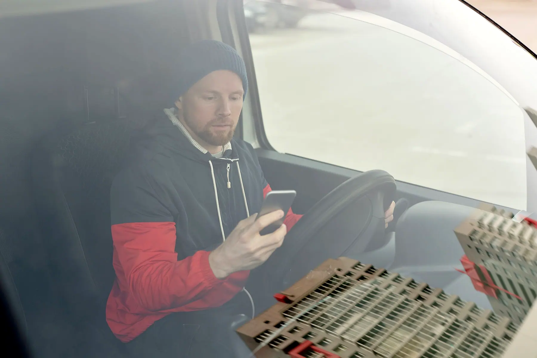 A man in a beanie sitting in the driver's seat of a van, typing on his phone