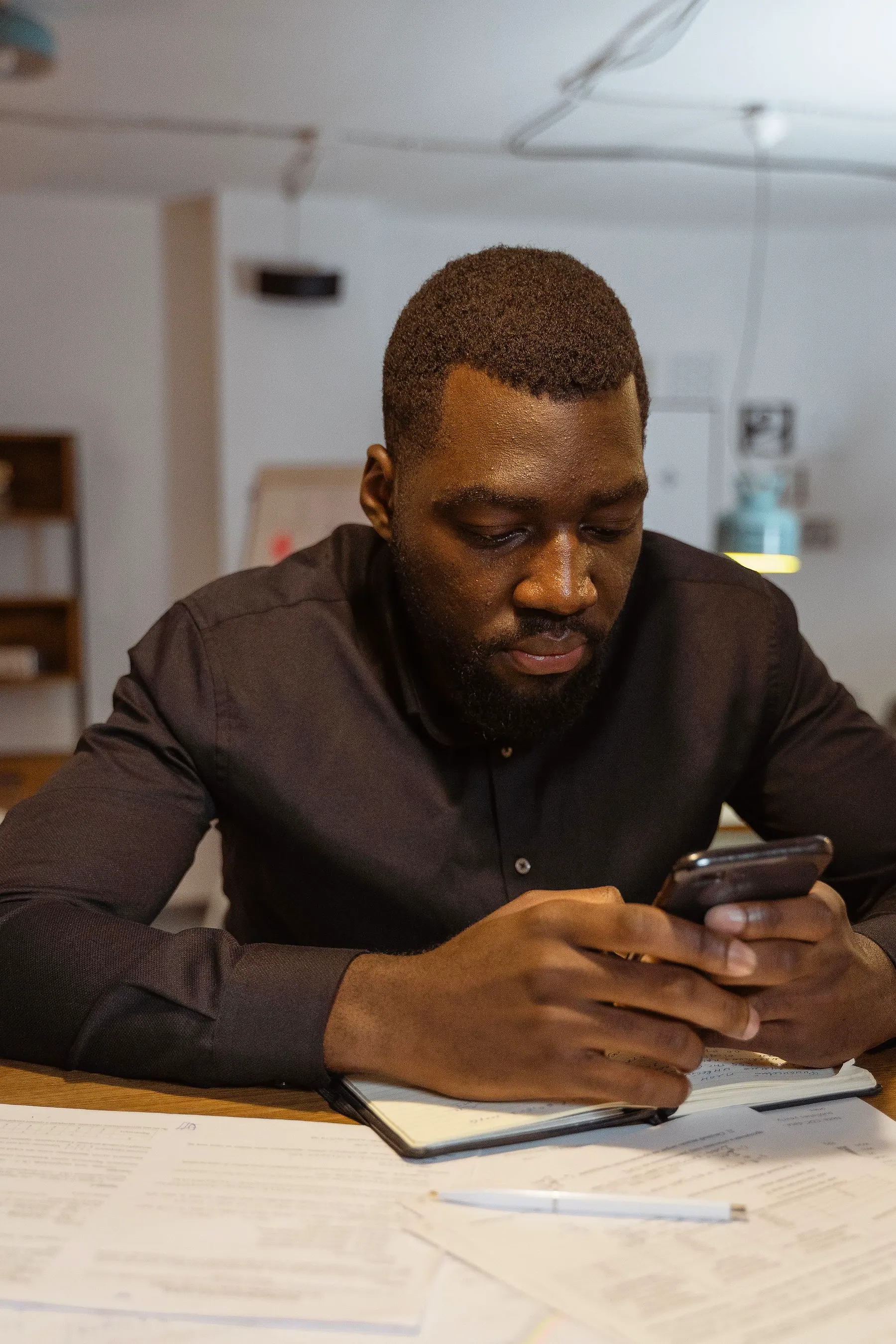 A man sitting at a desk with papers, typing a message on his phone