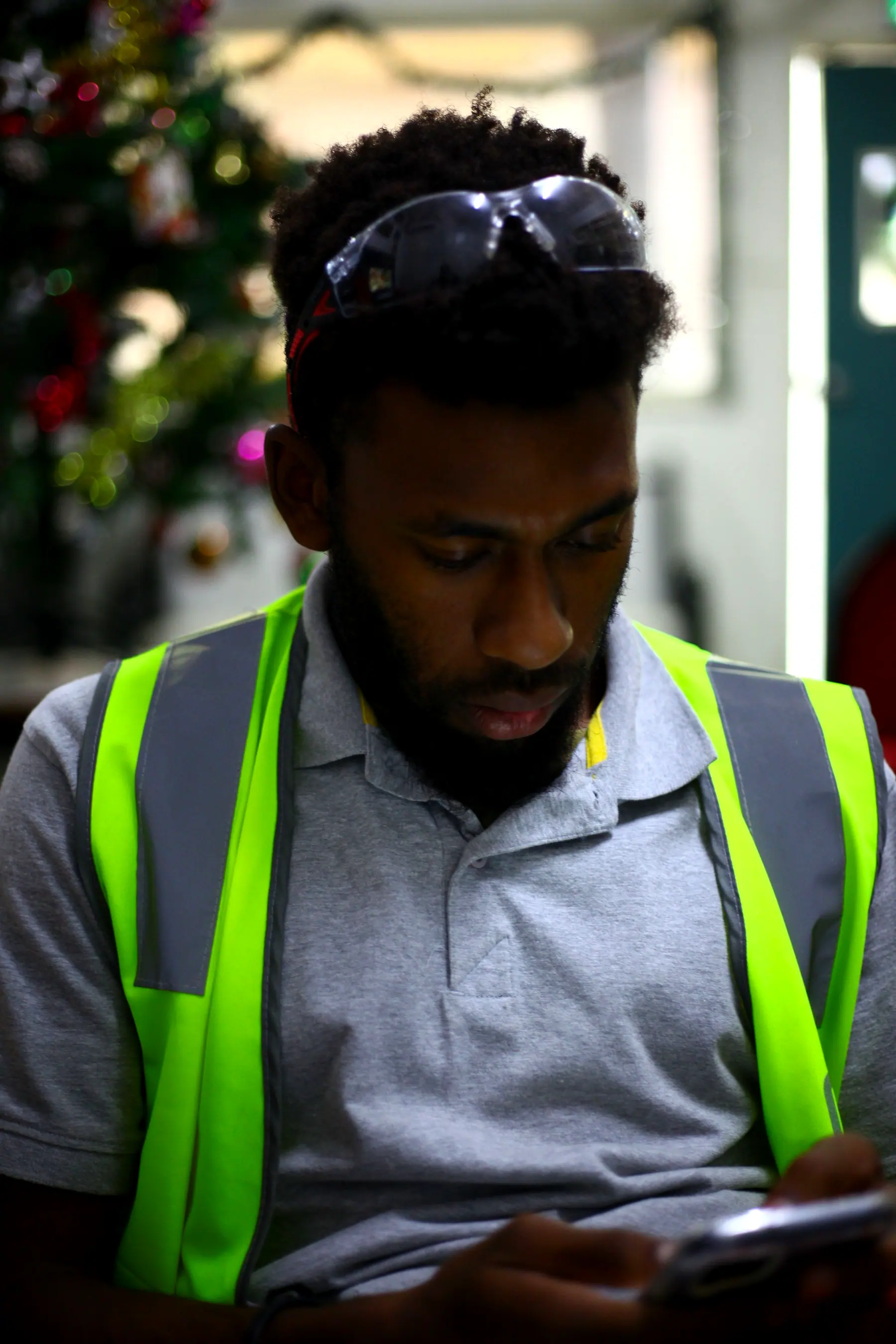 A man in a hi-vis vest looking down at his phone indoors