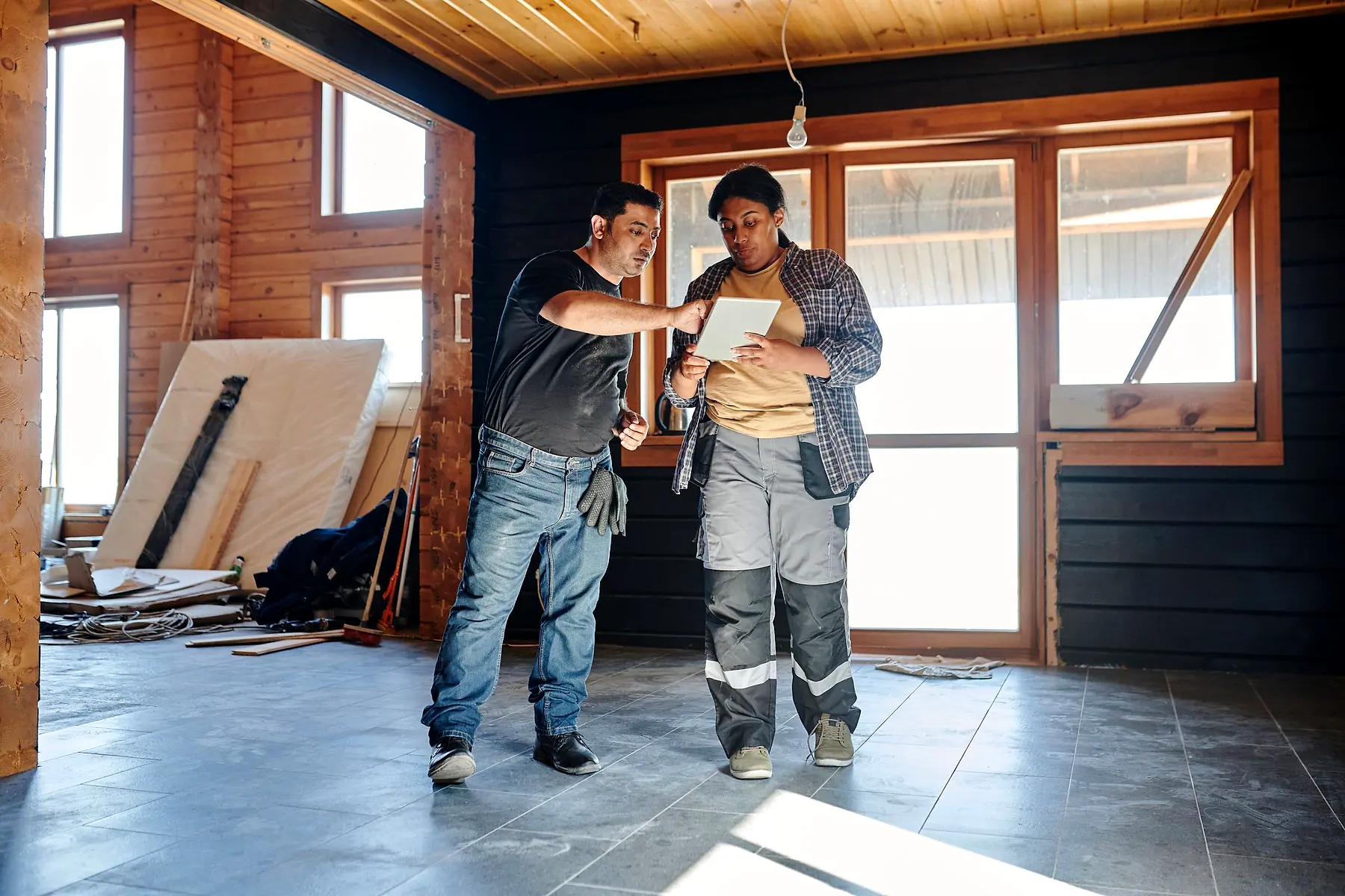 Two contractors in an unfinished timber room going over plans on a tablet